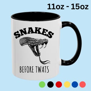 May include: A white ceramic mug with a black interior and handle, featuring a black graphic of a snake with its mouth open and fangs exposed. The text "SNAKES" is printed above the snake and "BEFORE TWATS" below it. The mug is available in 11oz and 15oz sizes.