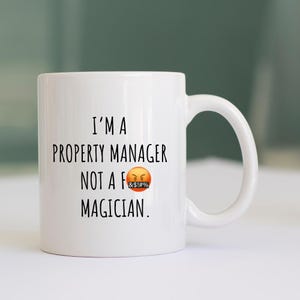 May include: White ceramic mug with a curved handle. The mug features black text that reads "I'M A PROPERTY MANAGER NOT A F&#$% MAGICIAN." An angry face emoji is included. The mug is designed for property managers.