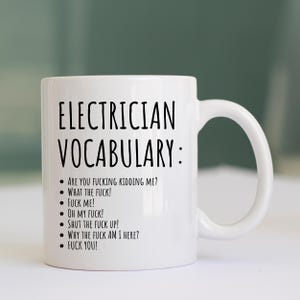 May include: White ceramic mug featuring the text "ELECTRICIAN VOCABULARY:" and a list of expletives. The mug has a curved handle and is suitable for hot or cold drinks. A humorous gift for electricians.