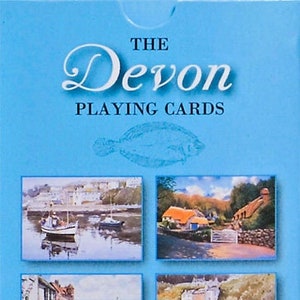 Pode incluir: Uma caixa de cartas de jogar com ilustrações cênicas de Devon, Inglaterra. A caixa é azul com texto branco que diz "The Devon Playing Cards". A parte frontal da caixa apresenta quatro imagens menores de cenas pitorescas de Devon, incluindo um porto com barcos, uma vila pitoresca, uma cena costeira e um porto com barcos.