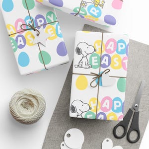 May include: White Easter-themed gift wrap with colorful polka dots and the words "Happy Easter." Some packages are tied with twine and adorned with wooden star and heart-shaped tags. A spool of twine and scissors are also present.