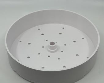 Könnte beinhalten: Weißer Plastik-Dampfkorb mit einem zentralen Loch und mehreren kleinen Löchern am Rand.