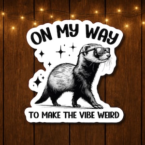 May include: A black and white sticker featuring a ferret wearing sunglasses. The sticker has the text "ON MY WAY TO MAKE THE VIBE WEIRD" in a bold, playful font. The design includes star accents, creating a fun and quirky aesthetic.