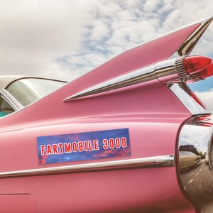 K&ouml;nnte beinhalten: Ein rosafarbenes Oldtimer-Auto mit einer verchromten Heckflosse und einem Sto&szlig;f&auml;ngeraufkleber mit der Aufschrift "Fartmobile 3000".