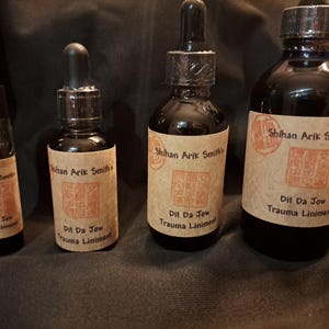May include: Four dark glass bottles of varying sizes, each with a brown label featuring text and a red stamp. The labels read "Shihan Arik Smith's Dit Da Jow Trauma Liniment."
