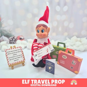 May include: A red and white elf doll with a red hat and striped legs, holding a boarding pass. Beside the elf are miniature suitcases, an easel sign, and an elf passport. The sign reads "I'm back again and ready for fun..."