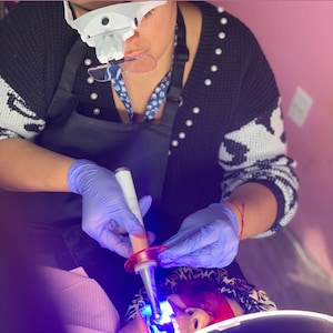 May include: A person wearing blue gloves uses a dental curing light to harden a filling on a patient's tooth.