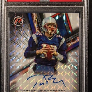 Può includere: Una carta di football di Tom Brady della serie 2023 Topps Composite, con un autografo. La carta è classificata GEM MT 10. La carta ha un design geometrico con il testo "CHASER!!" in basso.