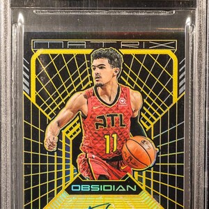 Peut inclure: Carte de basket-ball Trae Young de la série Panini Obsidian 2018-19, notée 9.5 Gem Mint. Elle présente une signature et un design noir et jaune avec le texte "CHASER!!".