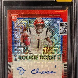 Puede incluir: Tarjeta de novato de Ja'Marr Chase calificada de la serie 2021 Panini Contenders Optic. La tarjeta presenta una foto del jugador con el uniforme de los Bengals, un diseño de boleto de novato y una firma. La tarjeta está en un soporte protector.