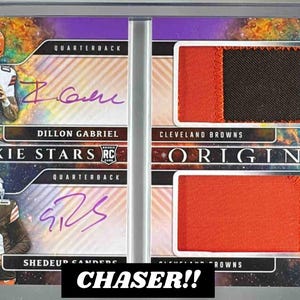 May include: A collectible sports card featuring Dillon Gabriel and Shedeur Sanders, both quarterbacks. The card includes player signatures and patches from Cleveland Browns jerseys. The text "ROOKIE STARS" and "ORIGINS" are visible, along with "CHASER!!".