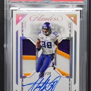 Puede incluir: Una tarjeta coleccionable 2023 Flawless Adrian Peterson dual patch auto-silver, calificada Gem Mint 10. La tarjeta presenta a un jugador con uniforme morado y blanco, con una firma y el texto "CHASER!!" en la parte inferior.