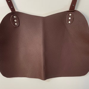 May include: Brown leather apron with two straps and silver rivets. The apron is folded in half.