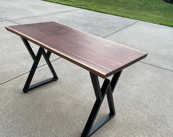 May include: A dark wood desk with a live edge top and black metal X-shaped legs.