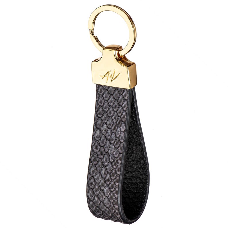 May include: A black leather keychain with a gold ring and a gold A+V logo. The leather has a snakeskin pattern.