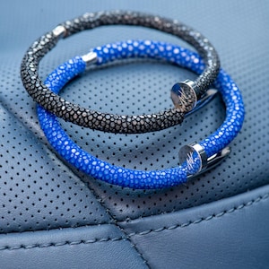 May include: Two leather bracelets with a silver clasp. The bracelet on top is black and the bracelet on the bottom is blue.