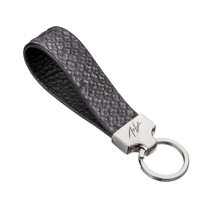 May include: A black leather key chain with a silver key ring and a silver tag with the signature "A.T." on it.