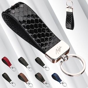 May include: A black leather keychain with a silver metal ring and a silver metal tag with the word "Nish" engraved on it. The keychain has a snakeskin pattern.