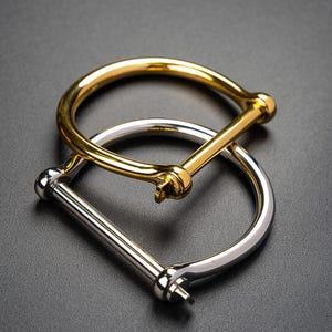 May include: Two metal bracelets, one gold and one silver, with a unique clasp design. The bracelets are stacked on top of each other.