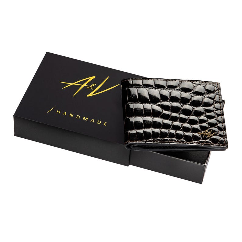 May include: A black leather wallet with a crocodile pattern and gold A&V logo. The wallet is in a black box with the text "A&V / HANDMADE" in gold lettering.