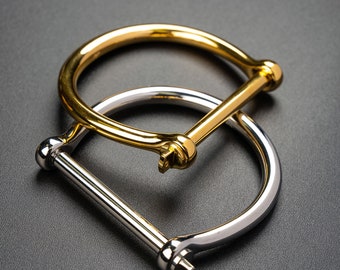 May include: Two metal bracelets, one gold and one silver, with a simple, minimalist design. The bracelets are both open and have a hinged clasp.