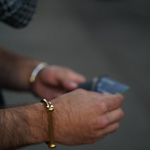 May include: A person wearing a gold bangle bracelet on their wrist. The bracelet has a simple design with two round ends.