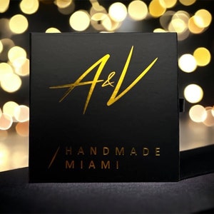 May include: A black box with gold lettering that reads "A&V Handmade Miami".