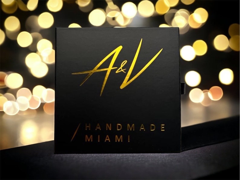 May include: A black box with gold lettering that reads "A&V Handmade Miami".
