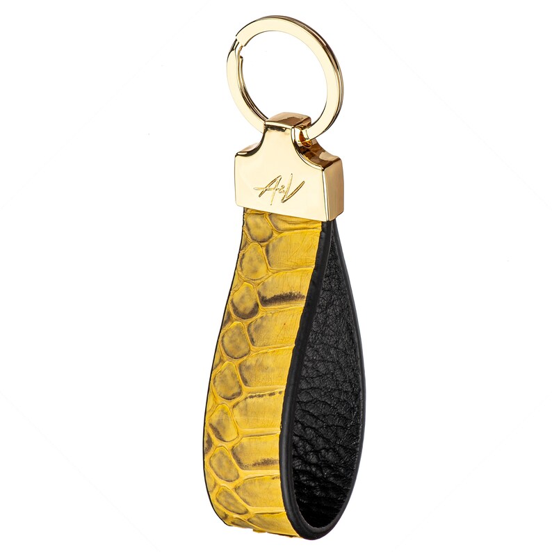 May include: A gold key chain with a yellow snakeskin leather strap and a black leather strap. The key chain has a gold ring and a gold tag with the initials "A.V."