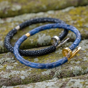 May include: Two leather bracelets, one black and one blue, with a gold nail clasp. The bracelets are made of stingray skin and are stacked on top of each other.