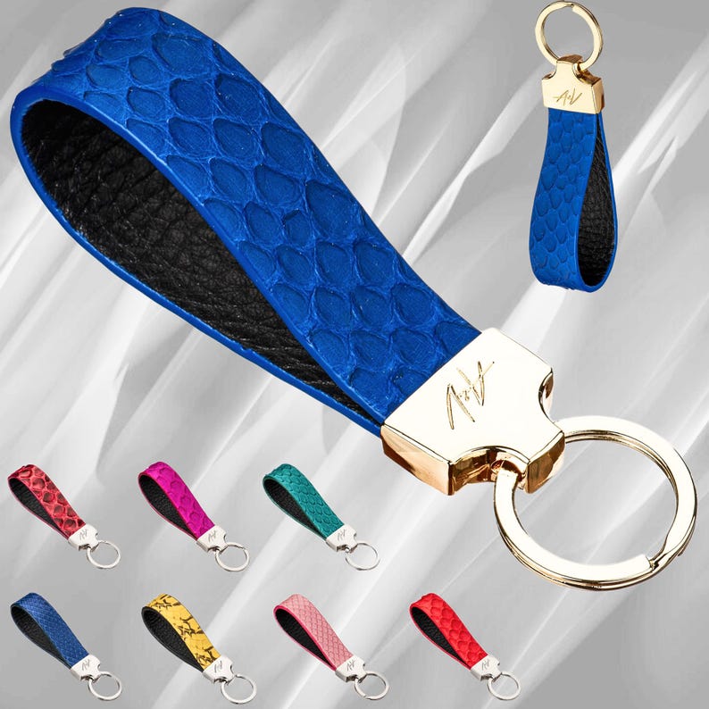 Może przedstawiać: Brązowy sk&oacute;rzany brelok do kluczy z złotym k&oacute;łkiem i złotą zawieszką z napisem "AV". Brelok wykonany jest ze sk&oacute;ry węża i ma czarne podłoże. W tle znajduje się dziewięć innych brelok&oacute;w w r&oacute;żnych kolorach.