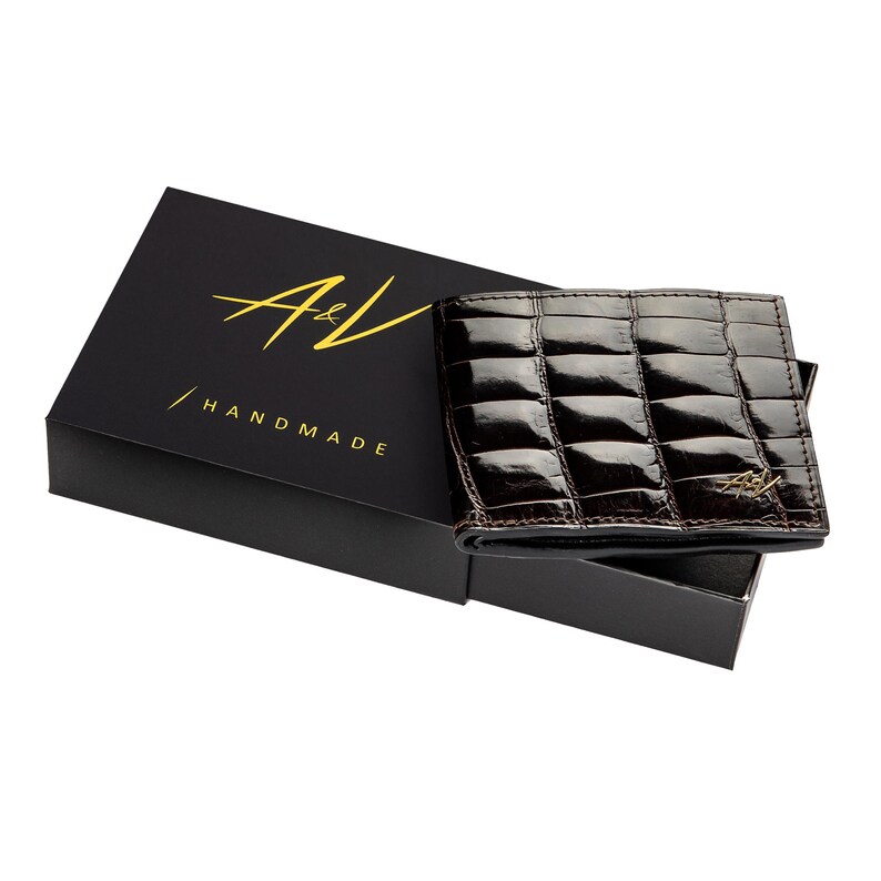 May include: A brown leather wallet with a crocodile pattern and gold A&V Handmade logo. The wallet is in a black box.