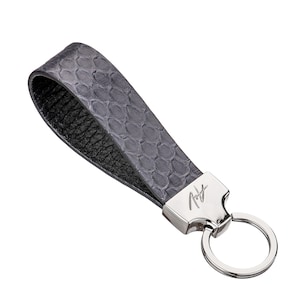 May include: A gray leather keychain with a silver key ring and a silver tag with the text "Roy" engraved on it.
