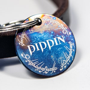 May include: A blue and orange metal dog tag with the inscription "PIPPIN" in white lettering. The tag is engraved with the inscription from the One Ring in Elvish script.