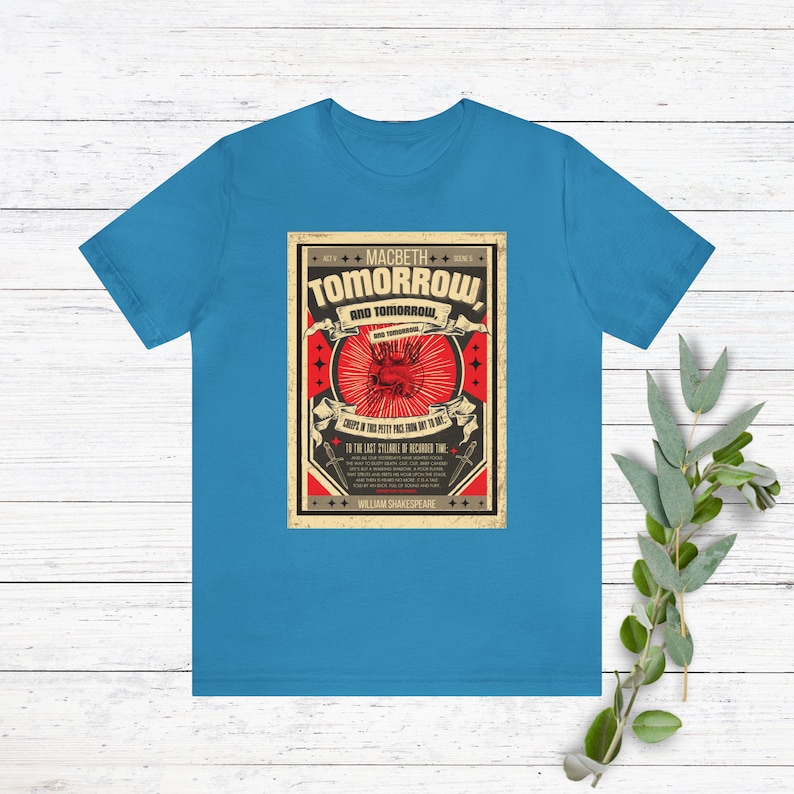 May include: A blue t-shirt with a vintage-style graphic featuring a red heart with a crown and the text "MACBETH TOMORROW AND TOMORROW, CREeps IN THIS PETTY PACE FROM DAY TO DAY... TO THE LAST SYLLABLE OF RECORDED TIME... WILLIAM SHAKESPEARE".