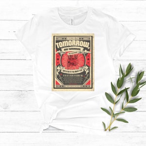 May include: A white t-shirt with a vintage-style graphic print featuring a red heart with a skull inside. The graphic includes the text "MACBETH TOMORROW AND TOMORROW, AND TOMORROW, CREeps IN THIS PETTY PACE FROM DAY TO DAY, TO THE LAST SYLLABLE OF RECORDED TIME, WILLIAM SHAKESPEARE".