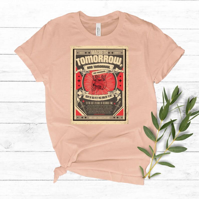 May include: A peach-colored t-shirt with a vintage-style graphic print featuring a red heart and the text "MACBETH TOMORROW AND TOMORROW" with a quote from Shakespeare's play Macbeth.