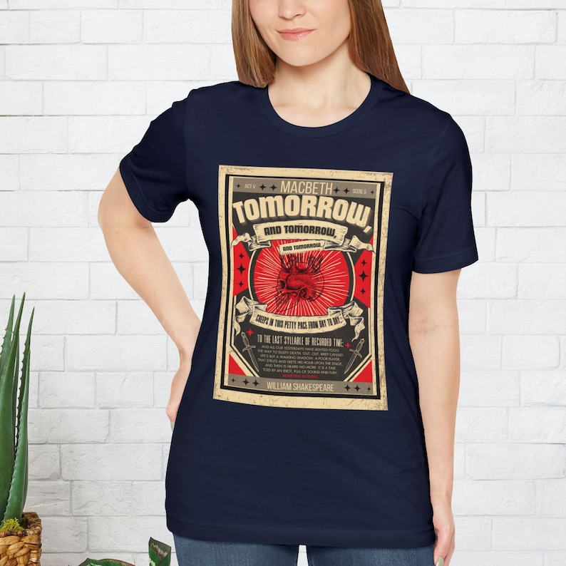 May include: A navy blue t-shirt with a vintage-style graphic of a skull and crossbones with the text "MACBETH TOMORROW AND TOMORROW" and a quote from the play. The graphic is in red, white, and black with a yellow background.