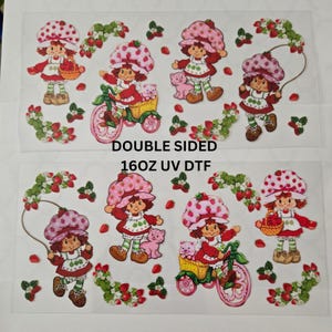 May include: Sheet of double-sided UV DTF transfers featuring Strawberry Shortcake characters. The designs include Strawberry Shortcake in various poses, with a bicycle, a basket, and a pink cat. The text "DOUBLE SIDED" and "16OZ UV DTF" is visible.