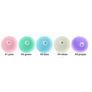 Op de afbeelding: Vijf ronde plastic deksels in verschillende kleuren: roze, groen, blauw, wit en paars. Elk deksel heeft een klein gaatje in het midden.