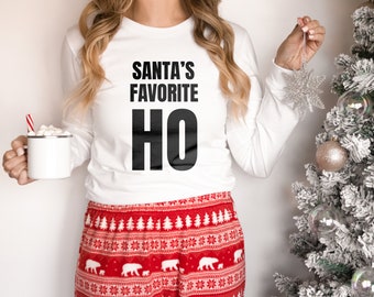 May include: White long-sleeved shirt with the text "Santa's Favorite Ho" printed in black. The person is wearing red and white patterned pajama pants.