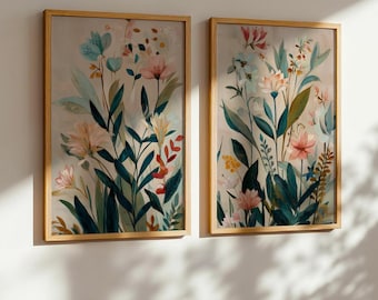 Può includere: Due stampe artistiche floreali incorniciate. Ogni stampa presenta un dipinto ad acquerello di fiori e fogliame colorati nelle tonalità del rosa, blu, giallo e verde. Le cornici sono in legno chiaro e lo sfondo è beige neutro.