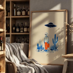 Retro alien UFO wall art featuring a quirky extraterrestrial walking through a desert landscape with cactus plants under a hovering spaceship. Bold blue and orange accents add a playful modern touch to the minimalist sci-fi illustration. Perfect for game rooms, living rooms, or offices, this unique artwork brings humor, character, and a creative sci-fi vibe to any interior. Ideal for space lovers and geek decor.