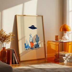 Retro alien UFO wall art featuring a quirky extraterrestrial walking through a desert landscape with cactus plants under a hovering spaceship. Bold blue and orange accents add a playful modern touch to the minimalist sci-fi illustration. Perfect for game rooms, living rooms, or offices, this unique artwork brings humor, character, and a creative sci-fi vibe to any interior. Ideal for space lovers and geek decor.
