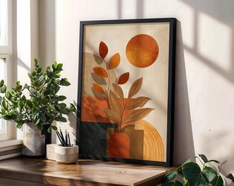Può includere: Stampa artistica astratta incorniciata con una calda tavolozza di colori. L'opera presenta una pianta stilizzata con foglie arancioni e marroni, un grande cerchio arancione e forme geometriche. La stampa è esposta su una superficie di legno vicino a una finestra.