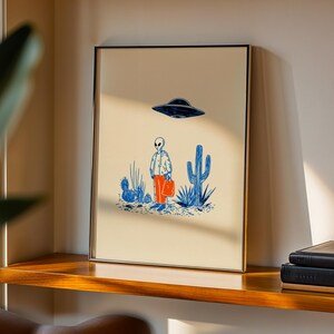 Retro alien UFO wall art featuring a quirky extraterrestrial walking through a desert landscape with cactus plants under a hovering spaceship. Bold blue and orange accents add a playful modern touch to the minimalist sci-fi illustration. Perfect for game rooms, living rooms, or offices, this unique artwork brings humor, character, and a creative sci-fi vibe to any interior. Ideal for space lovers and geek decor.