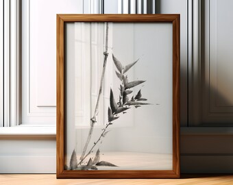 Puede incluir: Una obra de arte enmarcada con una pintura minimalista a tinta de tallos y hojas de bambú. La obra de arte está en un marco de madera y descansa sobre un suelo de madera. El bambú está representado en tonos grises y negros sobre un fondo blanco.