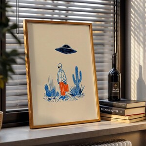 Retro alien UFO wall art featuring a quirky extraterrestrial walking through a desert landscape with cactus plants under a hovering spaceship. Bold blue and orange accents add a playful modern touch to the minimalist sci-fi illustration. Perfect for game rooms, living rooms, or offices, this unique artwork brings humor, character, and a creative sci-fi vibe to any interior. Ideal for space lovers and geek decor.