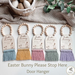 May include: Five wooden Easter bunny door hangers with a beaded garland and a tassel. Each hanger has the text "Easter Bunny Please Stop Here" and a small bunny illustration. The tassels are in blue, yellow, pink, green, and purple.