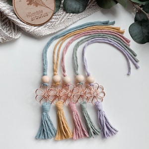 May include: Five colourful tassel keychains with wooden beads and a rose gold metal flower charm. The keychains are in shades of blue, yellow, pink, green, and purple.
